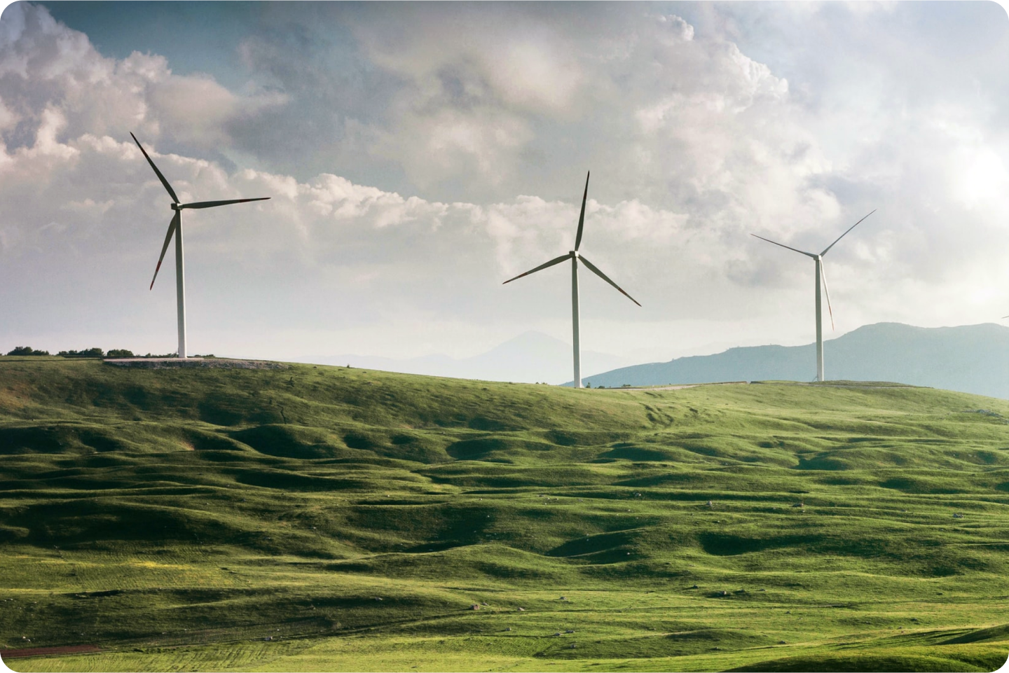 Três grandes turbinas eólicas no alto de uma colina com grama.